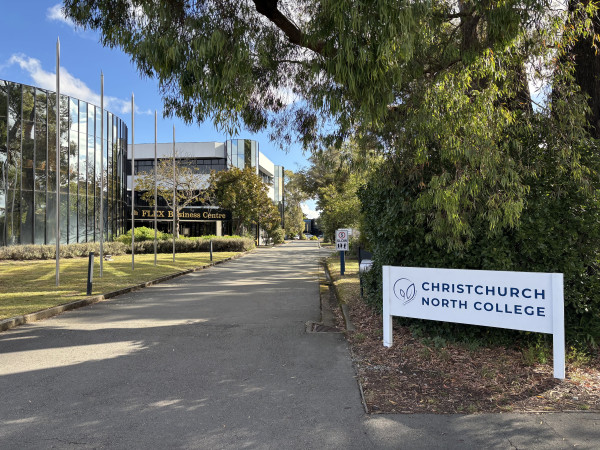 Photo shows the entrance to Christchurch North College. The bulk of the image shows a driveway with a building in the background. At the bottom right of the image is a white sign with dark blue text reading 'Christchurch North College.
